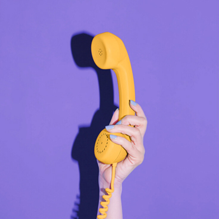 Hand hält gelben Telefonhörer vor lila Hintergrund