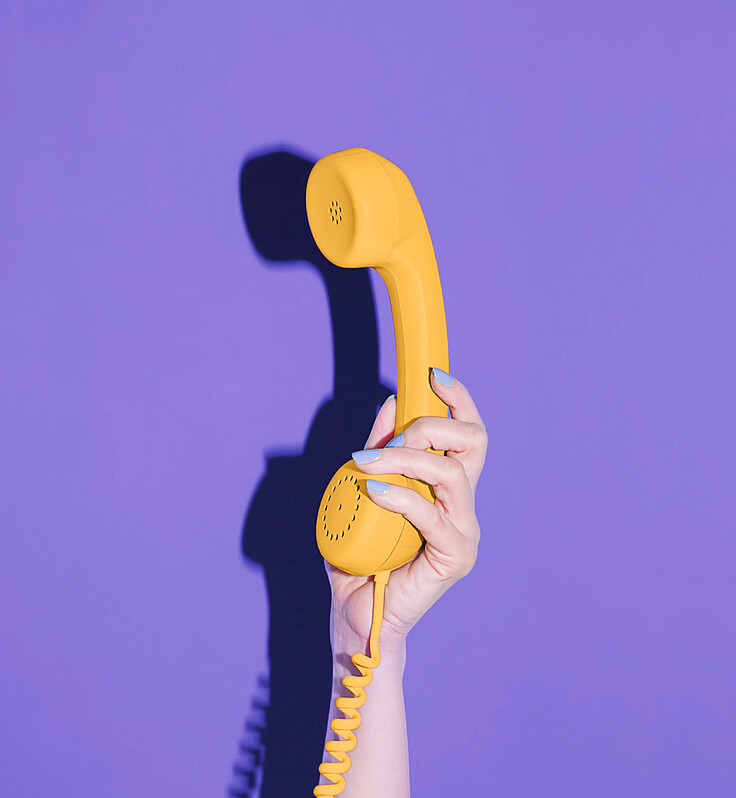Hand holding a yellow phone in front of purple background