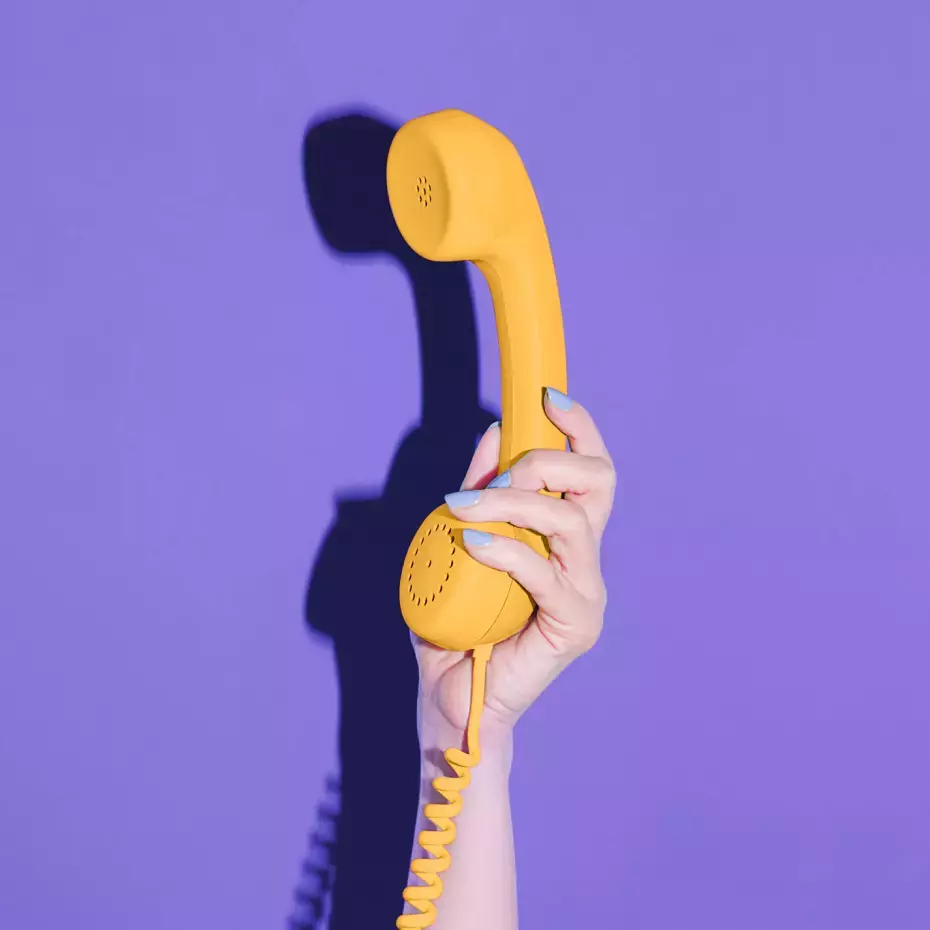 Hand hält gelben Telefonhörer vor lila Hintergrund